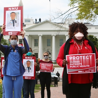 Masked nurse outside White House hold signs "Protect Nurses, Patients, Public Health"