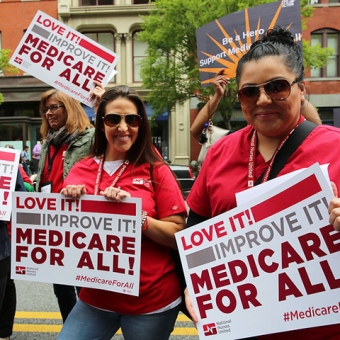 Two nurses outside holding signs "sign "Love it! Improve it! Medicare for all!"