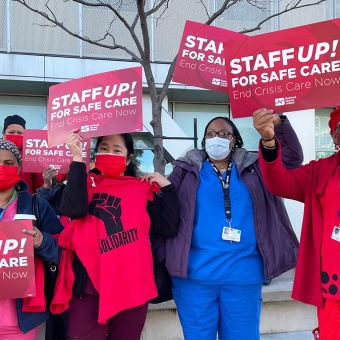 Group of nurses outside hold signs "Staff up for safe care"