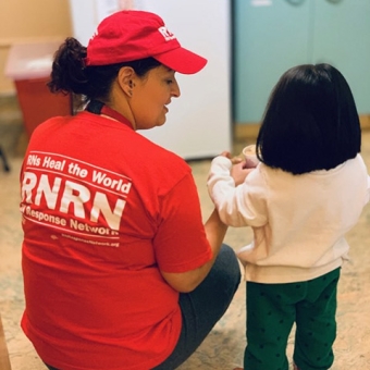 Nurse with RNRN t-shirt crouches nexr to toddler