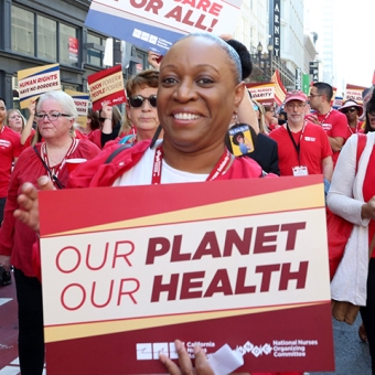 Nurse smiling, holding sign "Our Planet, Our Health"