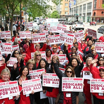 Large group of nurses outside holding Medicare for All signs