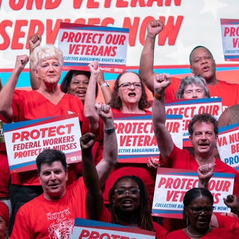 Large group of nurses with raised fists, holding signs "Protect Federal Workers, Protect VA Nurses"