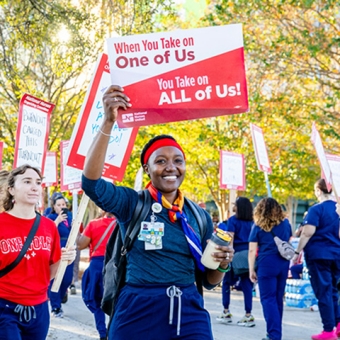 Nurse on picket line holding sign "When You Take On One Of Use, You Take On All Of Us"