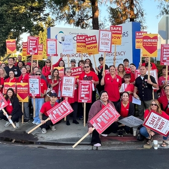 Large group of nurses outside hospital holding signs calling for safe staffing