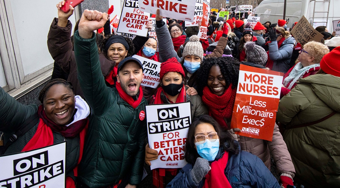 Large group of nurses cheering on picket line, some with raised fists