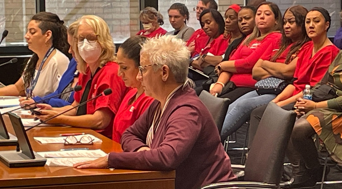 Group of nurses sitting at table with microphone for legislative hearing
