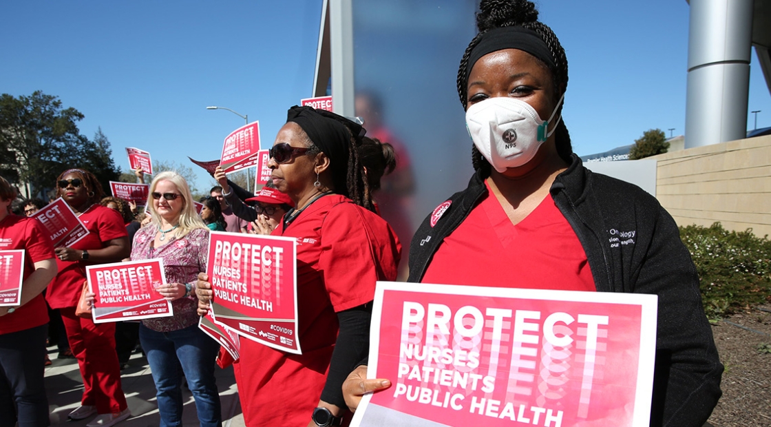 Nurses outside holding signs "Protect Nurses, Patients, Public Health"