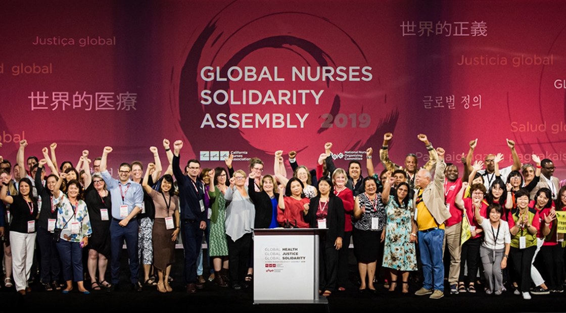 Large group of nurses on stage in front of banner "Global Nurses Solidarity Assembly"