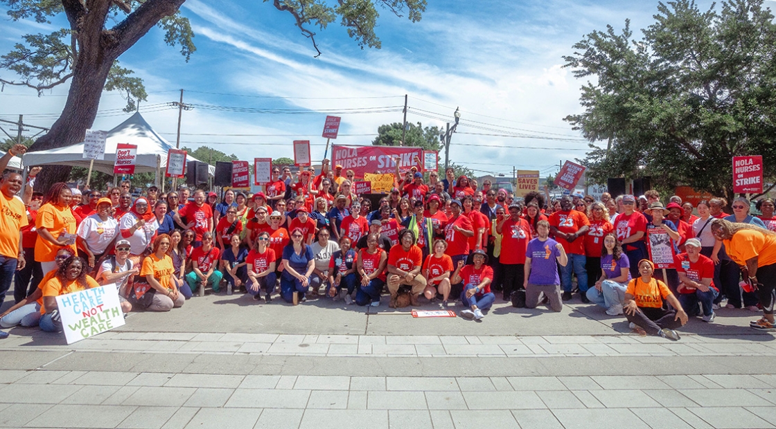 Large group of nurses outside behind banner "NOLA Nurses On Strike"