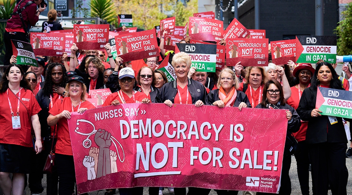 Large group of nurses marching, holding banner "Democracy is NOT for Sale"