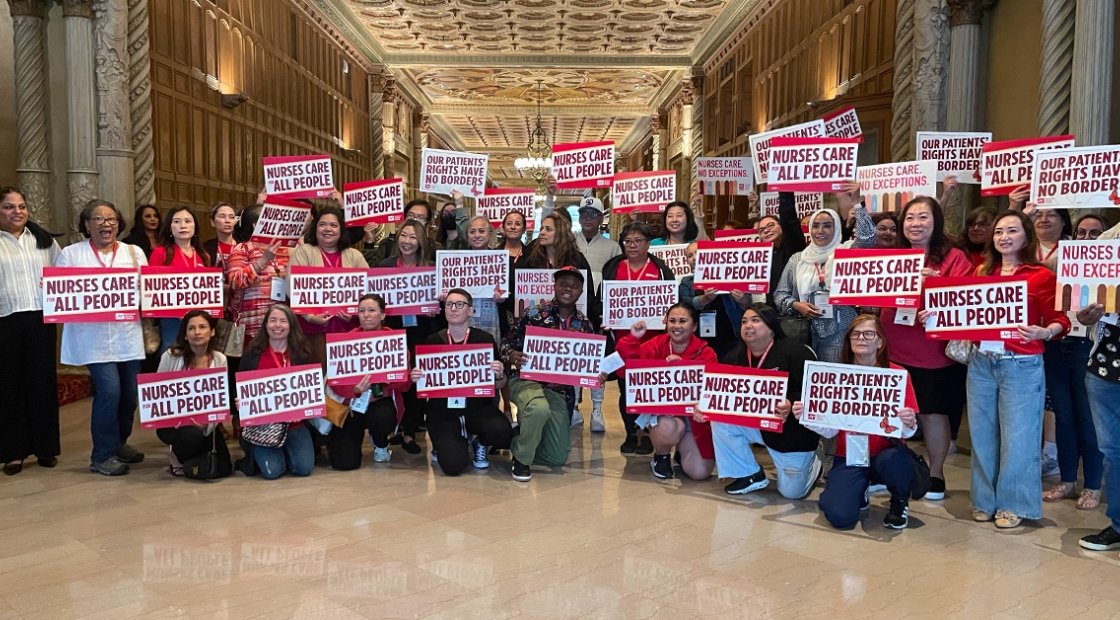 Large group of nurses inside, holding signs "Nurses care for all people"