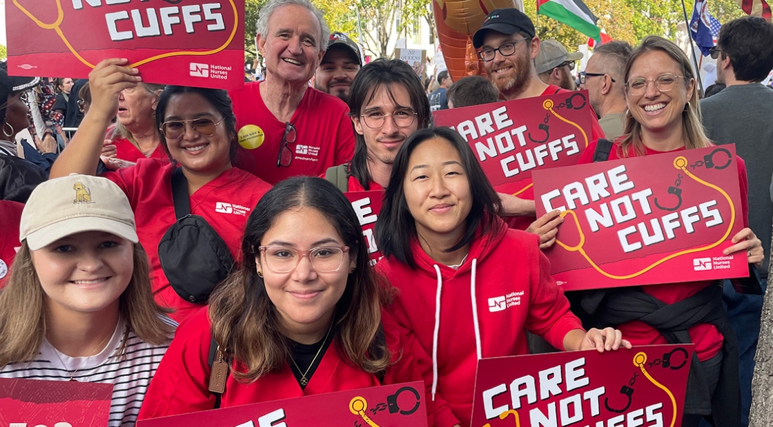 Group of nurses smiling, holding signs "Care Not Cuffs"