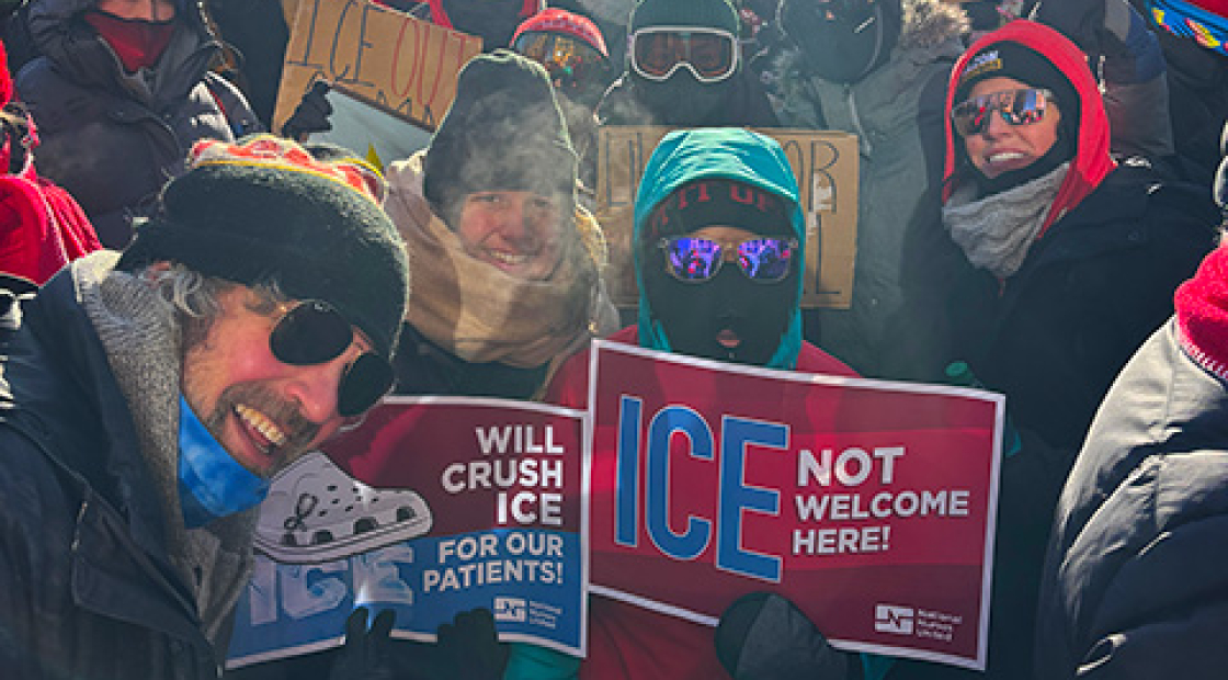 Group of nurses outside, wearing winter weather clothing, smiling, holding anti-ICE signs