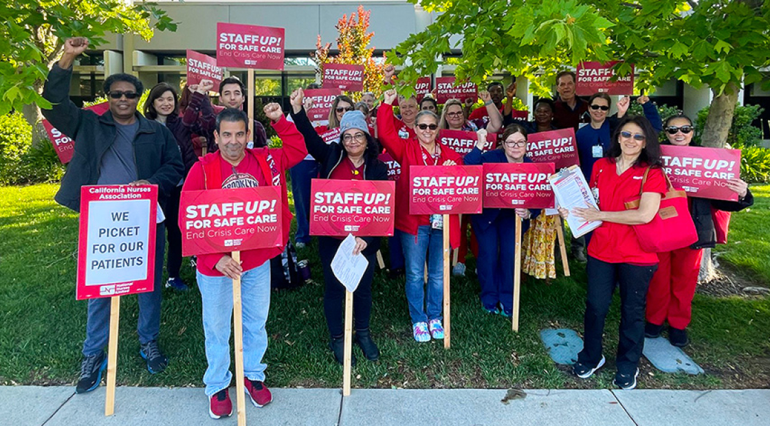 Large group of nurses outside hospital holding signs "Staff Up for Safe Patient Care"
