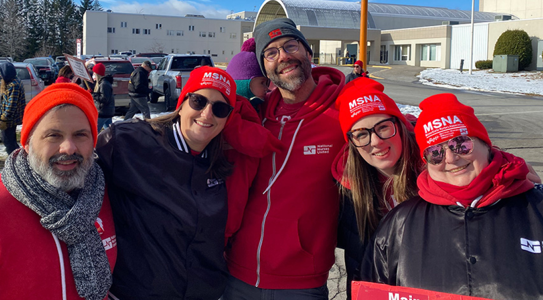 Five nurses outside hospital in cold weather clothes, smiling