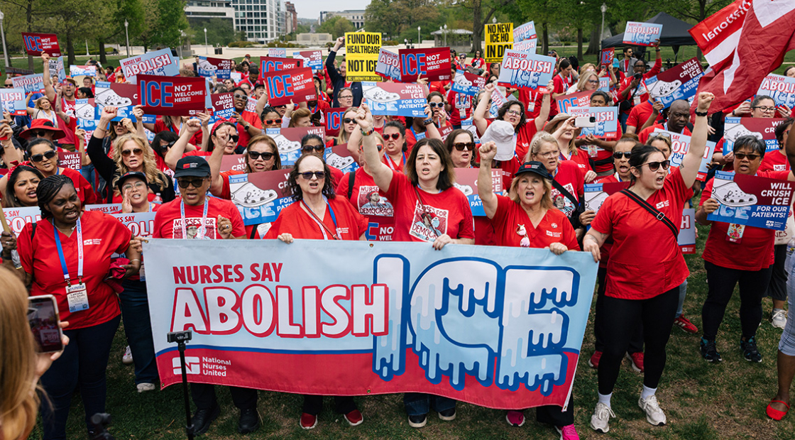 Large group of nurses outside, holding banner "Nurses Say Abolish ICE"