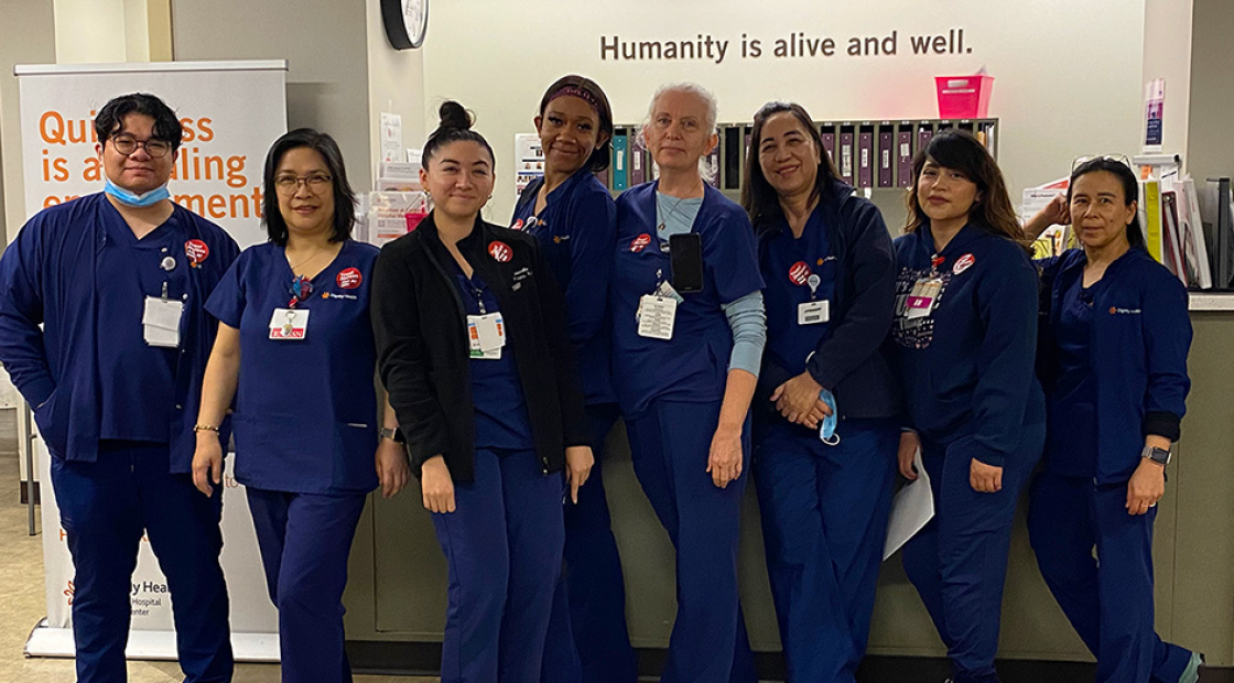 Group of eight nurses inside hospital, side-by-side, in blue scrubs