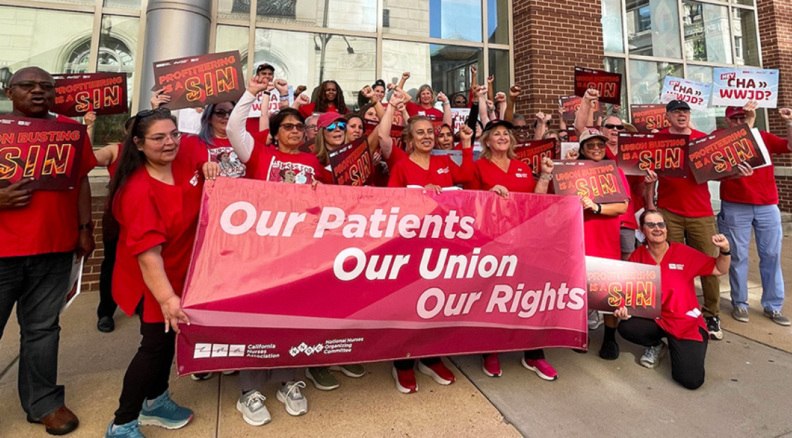 Group of nurses outside, holding banner "Our Patients, Our Union, Our Rights" and signs "Union Busting is a Sin"