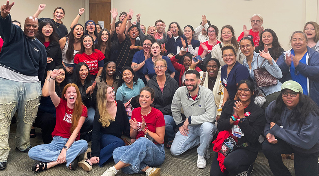 Large group of nurses inside hospital meeting room smiling with raised fists
