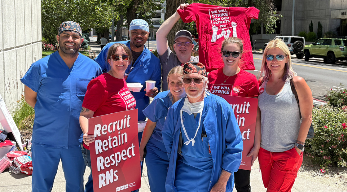 Nurses pose with pickets that read "Recruit, Retain, Respect RNs"