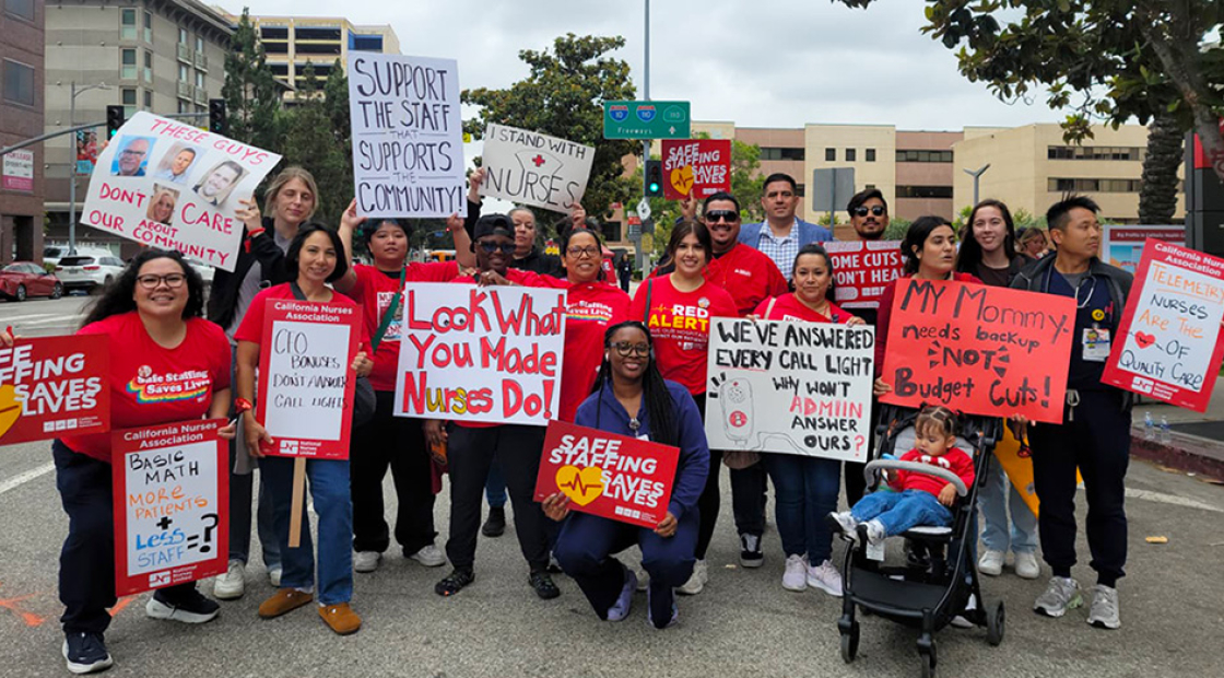 Large group of nurses outside hospital holding signs calling for patient safety and other measures