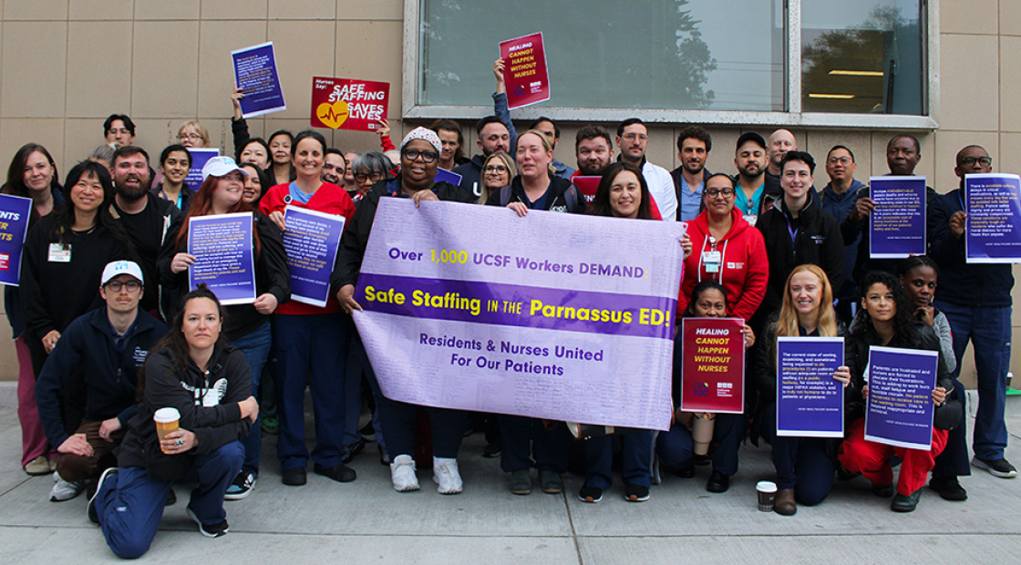 Group of nurses and physicians outside hospital holding banner "UCSF Workers Demand Safe Staffing"