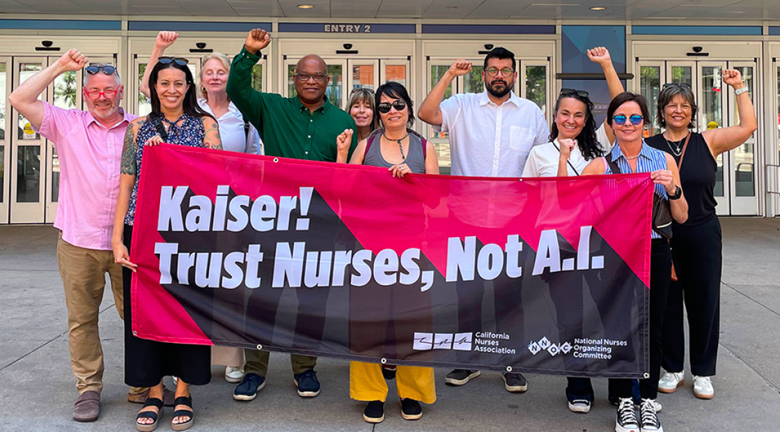 Group of nurses outside, with raised fists, holding banner "Kaiser! Trust Nurses, Not A.I."