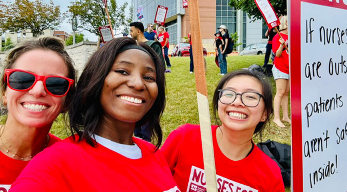 3 nurses outside hospital smiling, wearing red