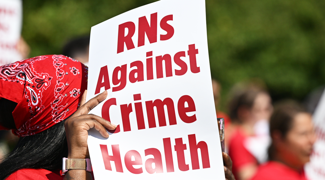Nurse holding/shading herself with sign "RNs Against Crime Health"