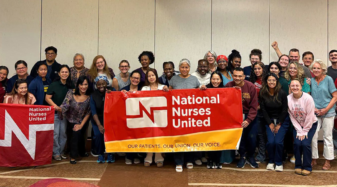 Large group of nurses inside conference room holding banner "National Nurses United"