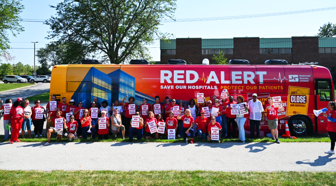 Nurses at Olympa Fields in front of Red Alert Tour bus with signs "Prime RNs United for Our Patients"