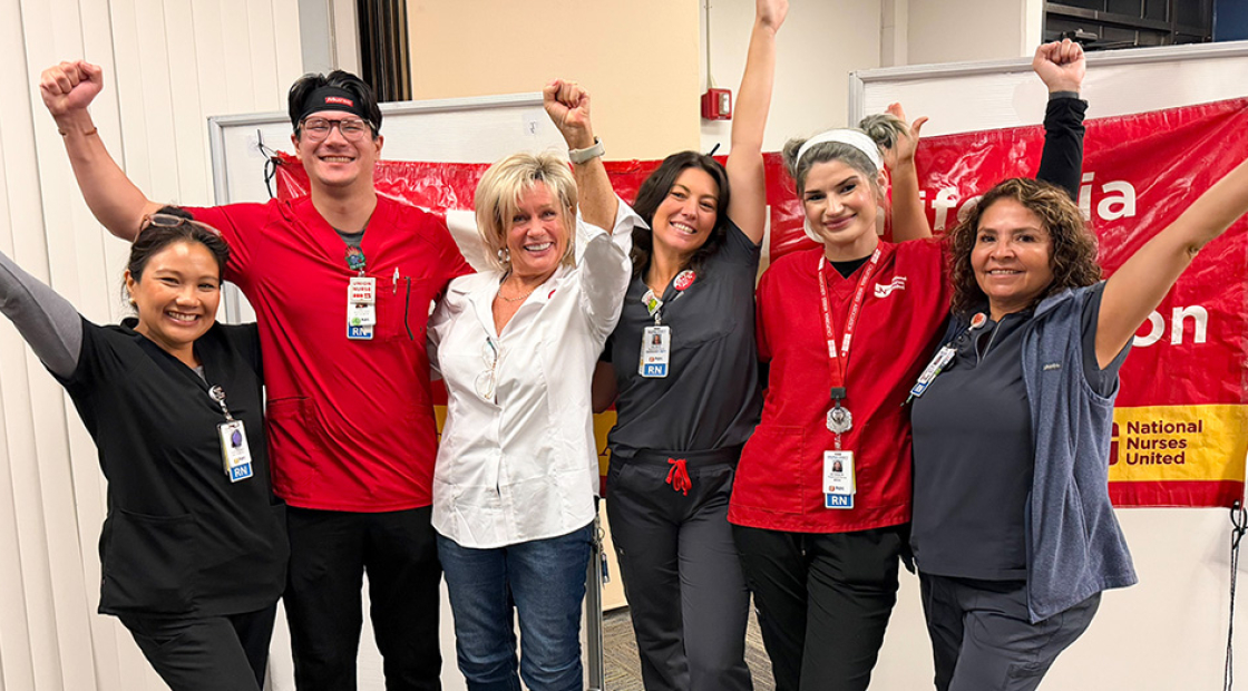 Six nurses inside, side-by-side, smiling, with raised arms/fists