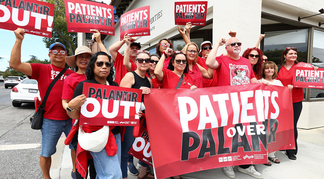 Group of nurses hold signs and banner "Palantir Out" and "Patients Over Palantir"