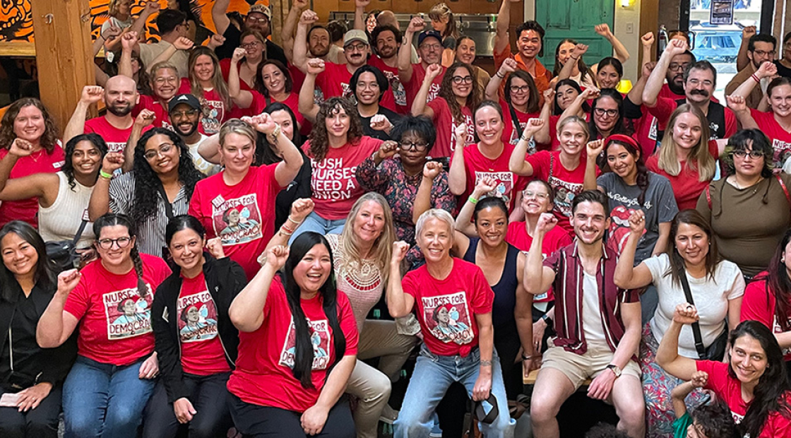 Large group of nurses inside, mostly wearing red, smiling, with raised fists