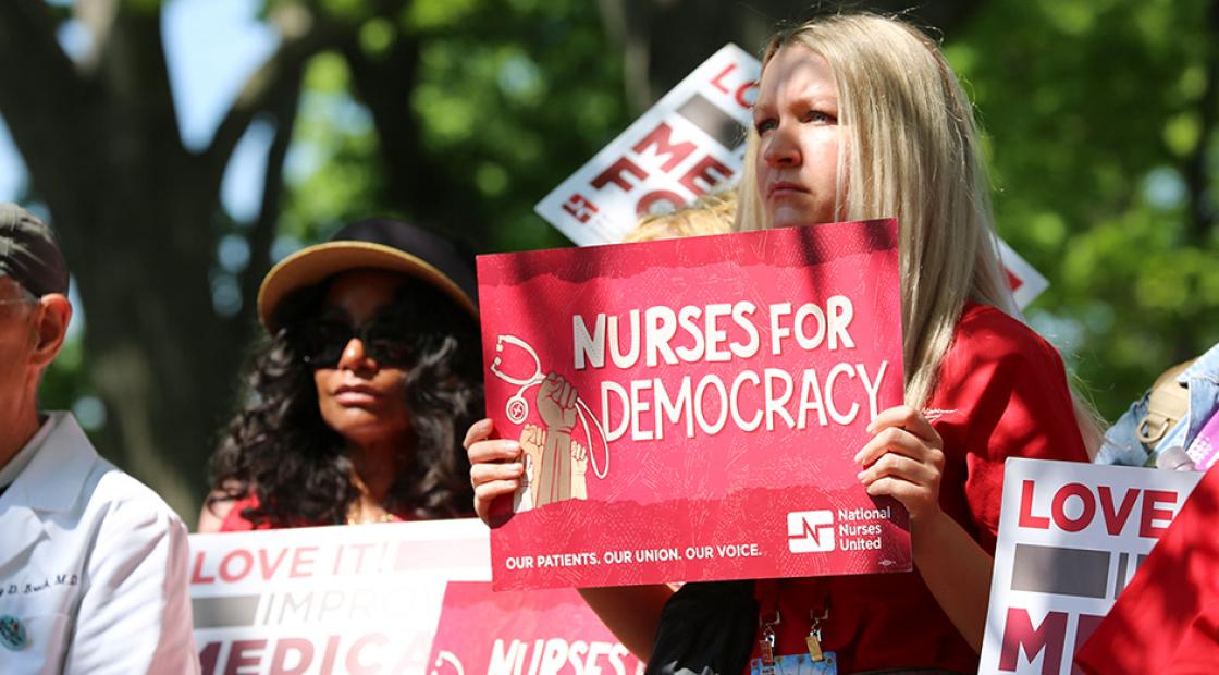 Nurse outside, holding sign "Nurses for Democracy"