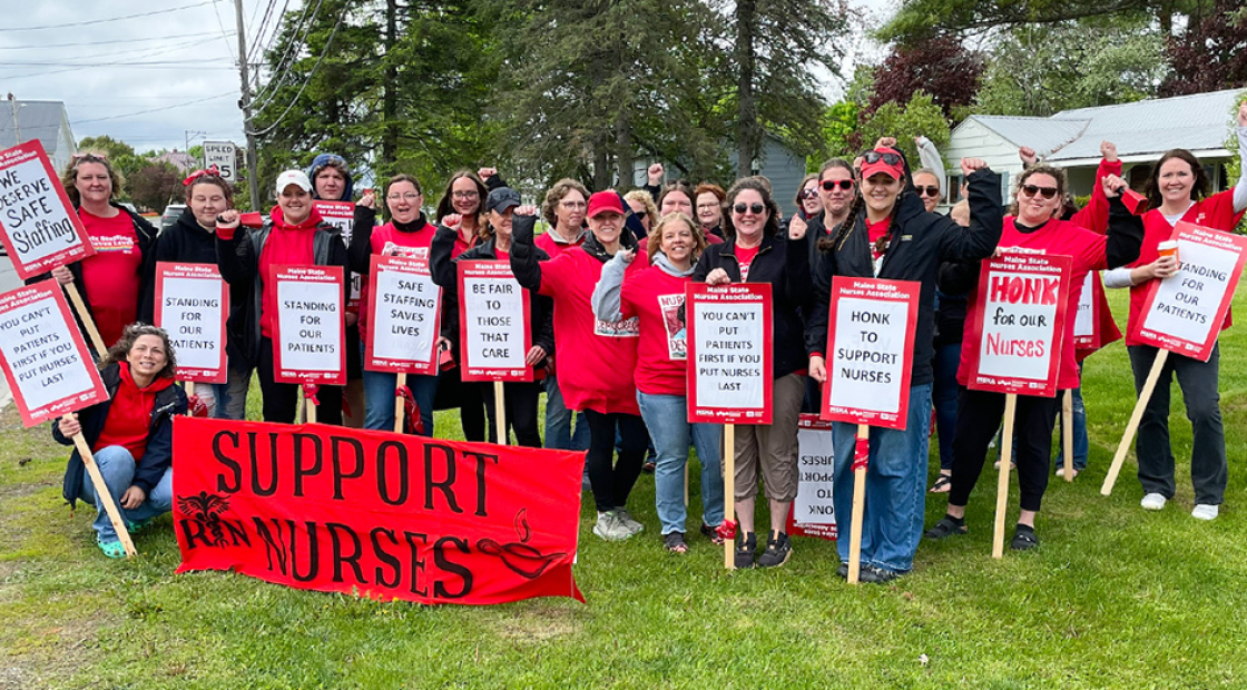 Large group of nurses outside, smiling, with raised fists, holding signs and banner "Support Nurses"