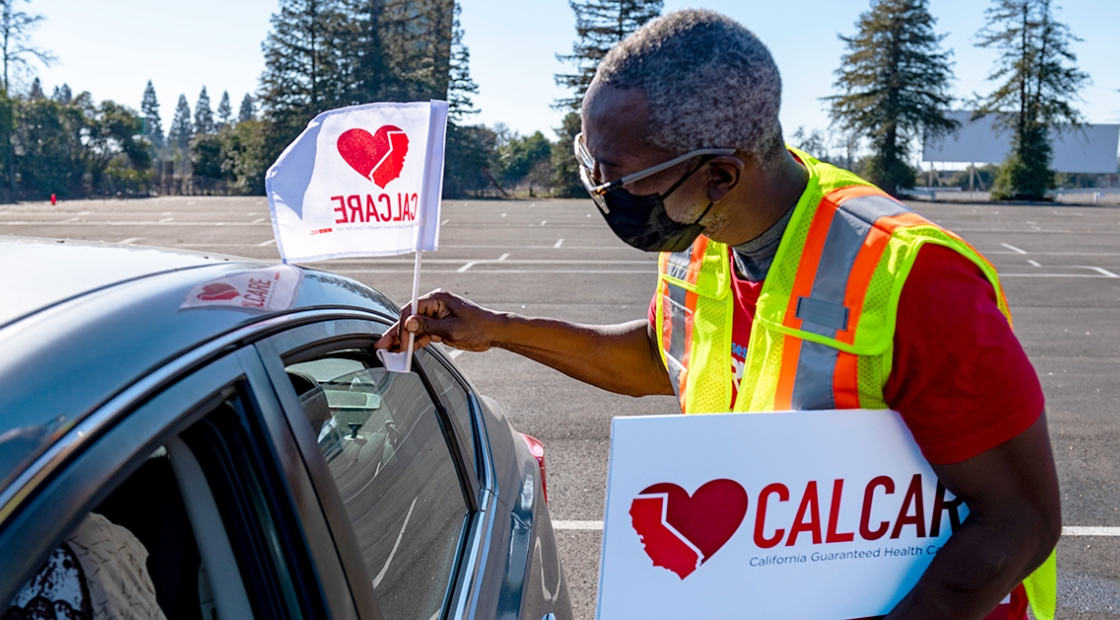 Person holding heart CalCare sign and placing flag on car.