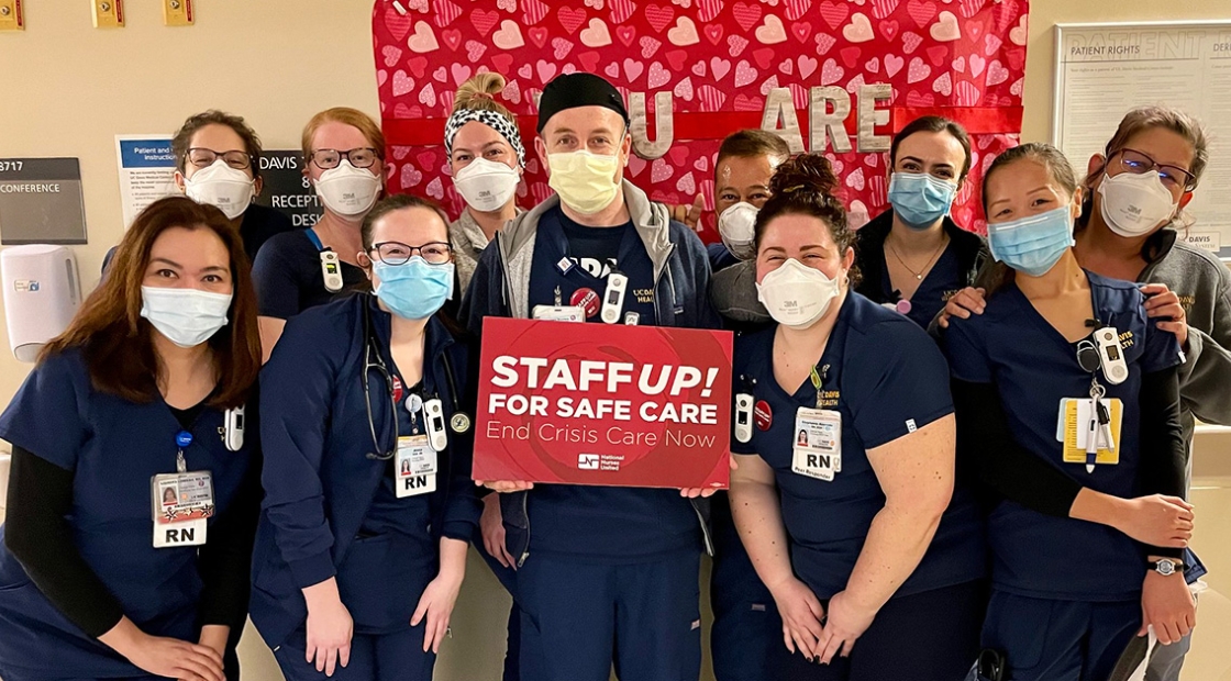 Large group of nurses inside hospital hold sign "Staff Up for Safe Care"