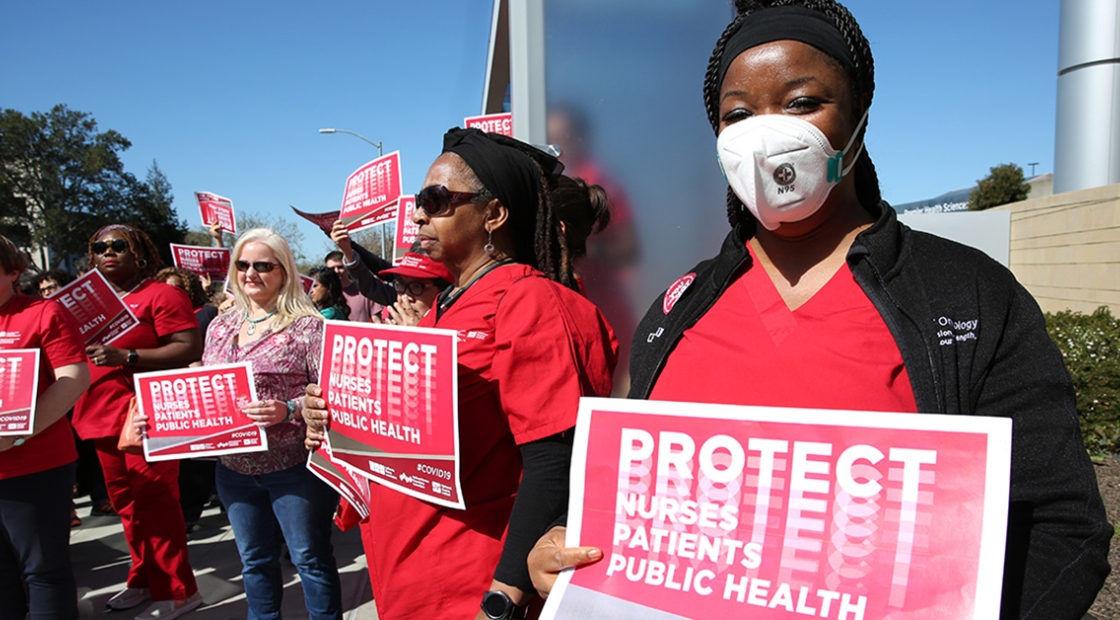 Nurses outside holding signs "Protect Nurses, Patients, Public Health"