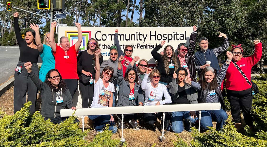Group of nurses in front of hospital smiling, with raised fists