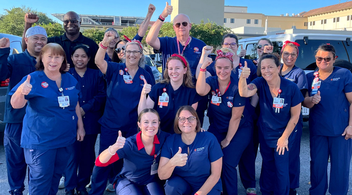 Large group of nurses outside hospital, smiling, with raised fists