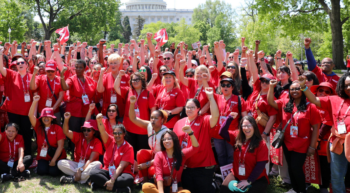 Large group of nurses outside capitol building, smiling, with raised fists