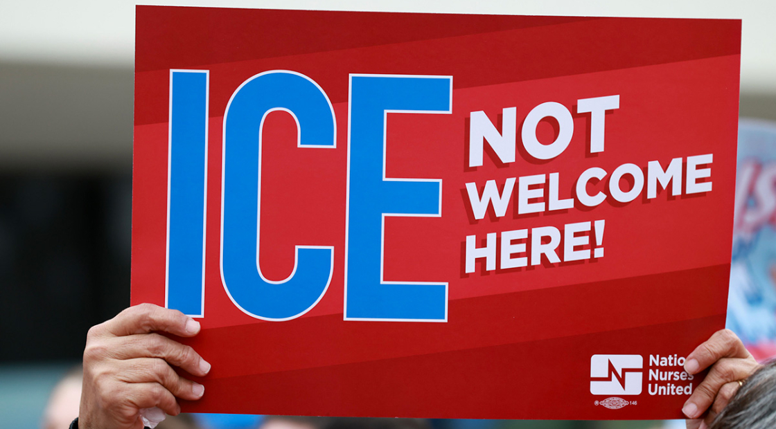 Hands holding sign "ICE Not Welcome Here"
