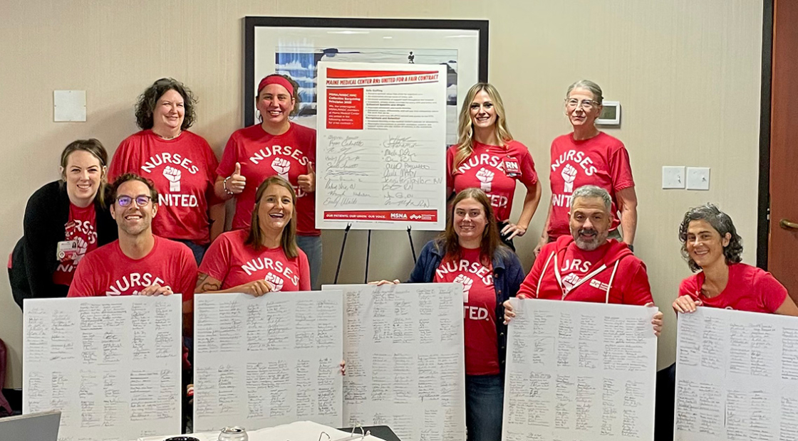 Group of nurses inside, holding large printouts of contract signers