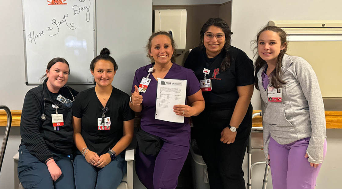 Group of five nurses inside hospital, smiling, giving thumbs up