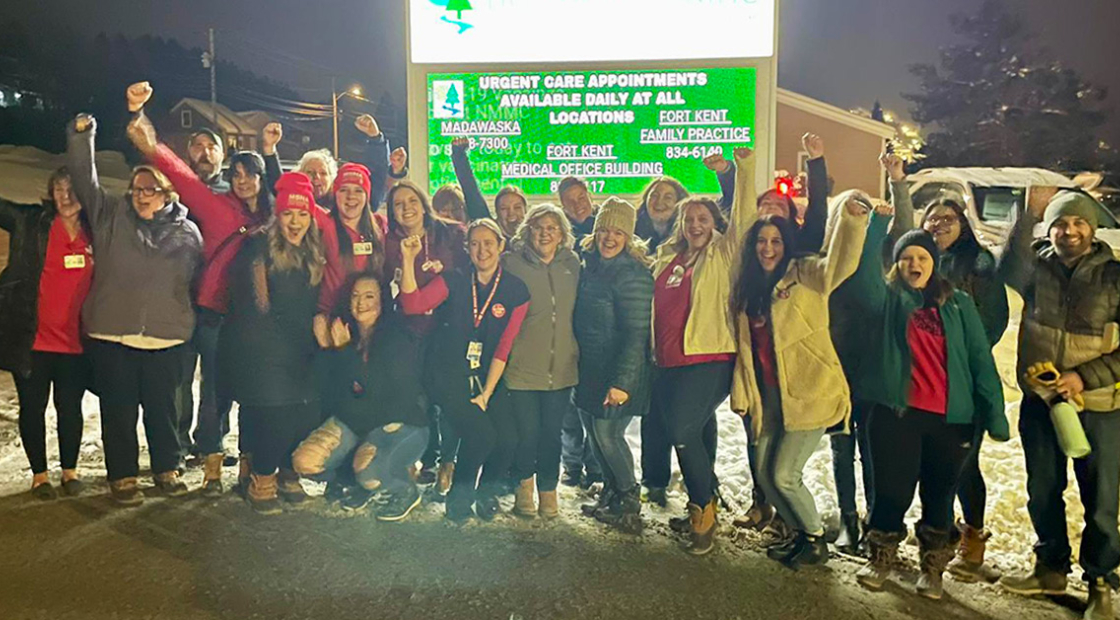 Large group of nurses outside hospital, smiling, with raised fists
