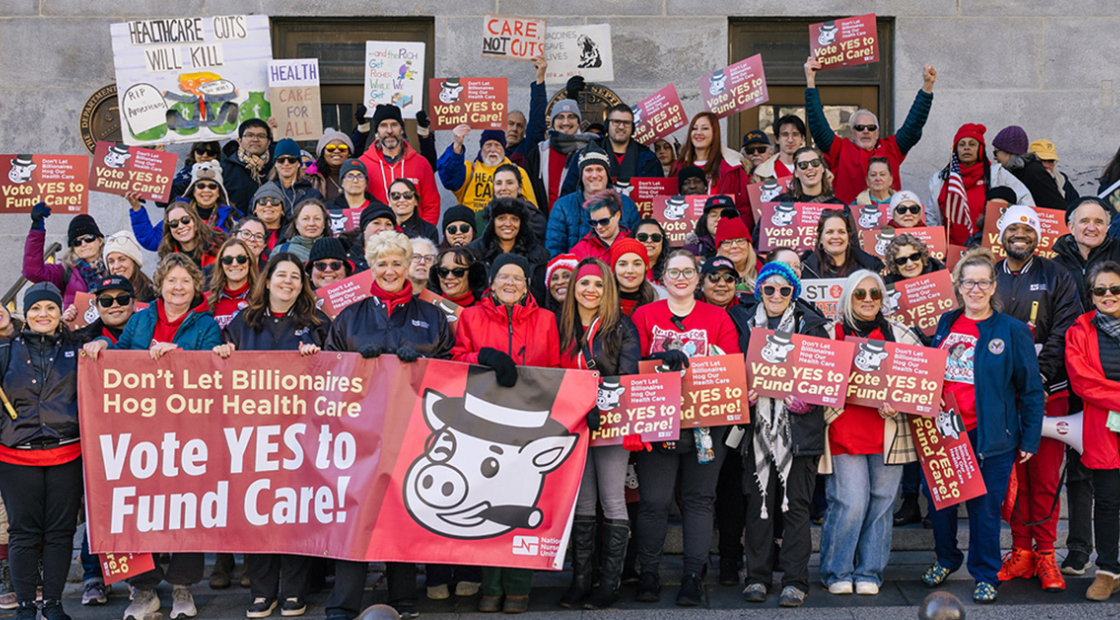 Large group of people holding banner and signs "Don't Let Billionairs Hog Our Health Care: Vote Yes to Fund Care"