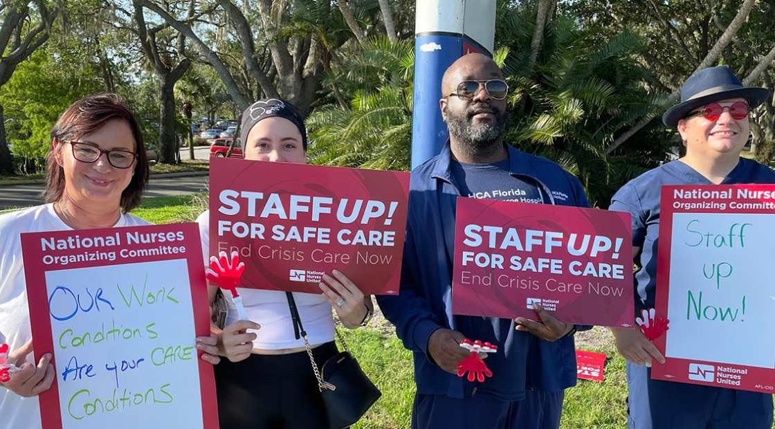 Four nurses outside hold signs "Staff Up for Safe Patient Care"