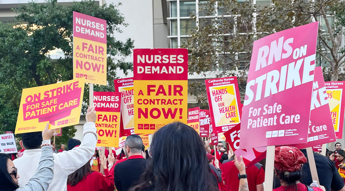 Nurses holding signs "RNs on strike for safe patient care" "Nurses demand a fair contract now!" "Hands off our health care"